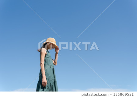 一位年輕女子穿著連身裙,背景是藍天。 一位年輕女子穿著連身裙,背景是藍天。 135969551