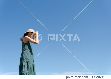 一位年輕女子穿著連身裙，背景是藍天。 135969553