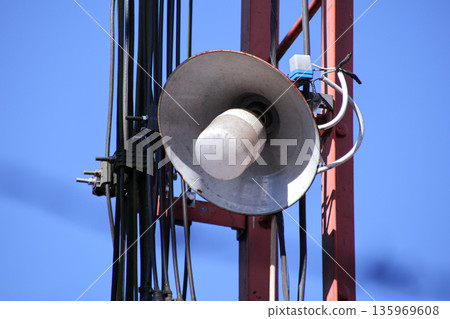 Loudspeaker mounted on a metal tower with a clear blue sky, emphasizing industrial communication and outdoor broadcasting capabilities 135969608