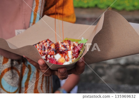 Indonesian Street Food Gado-Gado Being Prepared with Peanut Sauce Drizzle, a Traditional Dish Served in a Paper Bowl with Natural Light Indonesian Street Food Gado-Gado Being Prepared with Peanut Sauce Drizzle, a Traditional Dish Served in a Paper Bowl with Natural Light 135969632