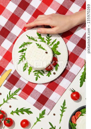 A hand places salad on a round plate with tomatoes A hand places salad on a round plate with tomatoes 135970269