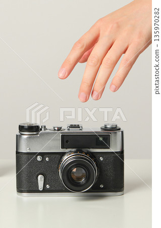 A hand extends toward a retro camera resting on a table A hand extends toward a retro camera resting on a table 135970282