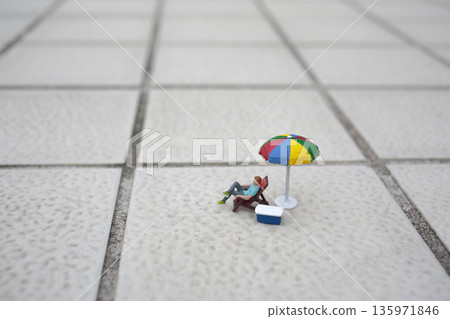Miniature Figure Relaxing Under Colorful Umbrella On Tiles Miniature Figure Relaxing Under Colorful Umbrella On Tiles 135971846