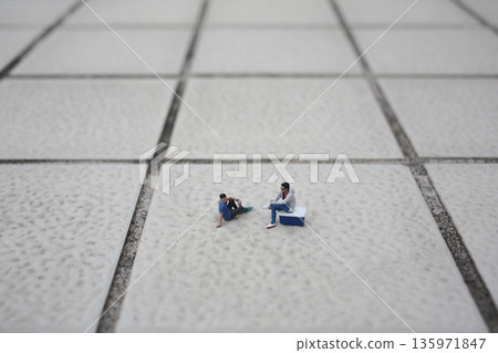 Tiny model people rest casually across wide textured tiles Tiny model people rest casually across wide textured tiles 135971847