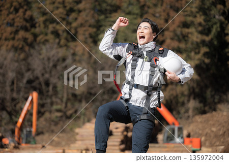 A man jumping at a height, wearing a helmet, with a shovel in the background at a construction site 135972004