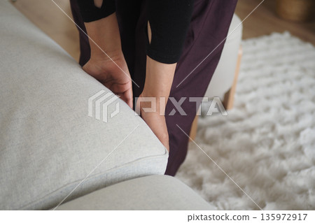 Person adjusting the cushion on a light sofa in a home Person adjusting the cushion on a light sofa in a home 135972917