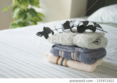Towels stacked on a bed with green leaves on top Towels stacked on a bed with green leaves on top 135972922