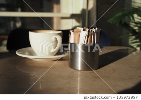 Coffee cup and sugar packets on a table in a cafe Coffee cup and sugar packets on a table in a cafe 135972957