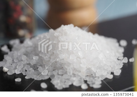 Salt sits on a black surface near spices and a container Salt sits on a black surface near spices and a container 135973041