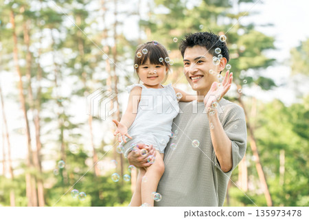 爸爸抱著小女孩在公園裡，親子情深，一家人（肥皂泡） 135973478