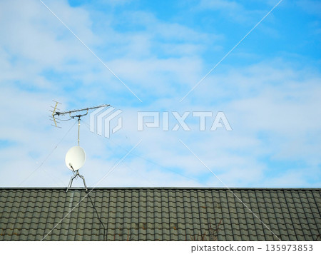 A refreshing blue sky and a tiled roof with a TV antenna on it 135973853