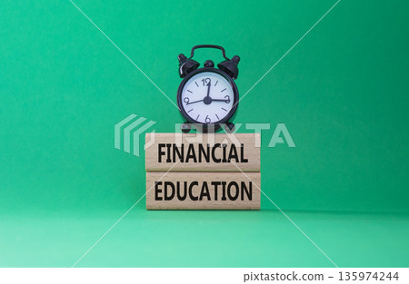 Financial Education symbol. Wooden blocks with words Financial Education. Beautiful green background with alarm clock. Business and Financial Education concept. Copy space. 135974244