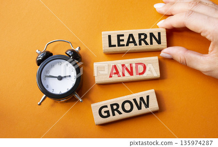 Learn and grow symbol. Concept words Learn and grow on wooden blocks. Businessman hand. Beautiful orange background with alarm clock. Business and Learn and grow concept. Copy space. 135974287