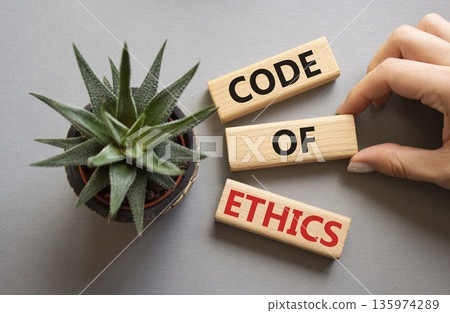 Code of ethics symbol. Concept words Code of ethics on wooden blocks. Businessman hand. Beautiful grey background with succulent plant. Business and Code of ethics concept. Copy space. 135974289