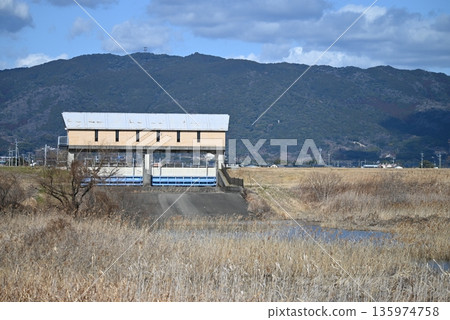 冬季，河床上矗立著一座大型防洪閘和排水設施，遠處環繞著群山。 135974758