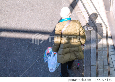 Yokohama cityscape in Japan: light and shadow... Aging society: An elderly woman with a cane (wearing a mask). On her way home from shopping, her left hand is gloved... 135976150