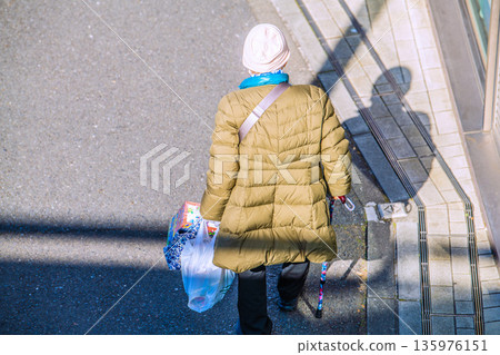 Yokohama cityscape in Japan: light and shadow... Aging society: An elderly woman with a cane (wearing a mask). On her way home from shopping, her left hand is gloved... 135976151