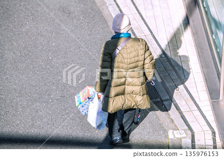 Yokohama cityscape in Japan: light and shadow... Aging society: An elderly woman with a cane (wearing a mask). On her way home from shopping, her left hand is gloved... 135976153