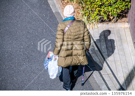 Yokohama cityscape in Japan: light and shadow... Aging society: An elderly woman with a cane (wearing a mask). On her way home from shopping, her left hand is gloved... 135976154