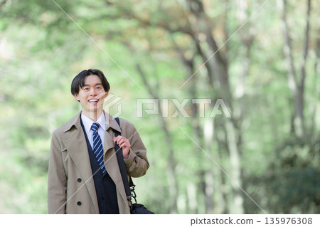 Smiling businessman on a job hunt or new graduate walking outside for sales with fresh greenery in the background 135976308