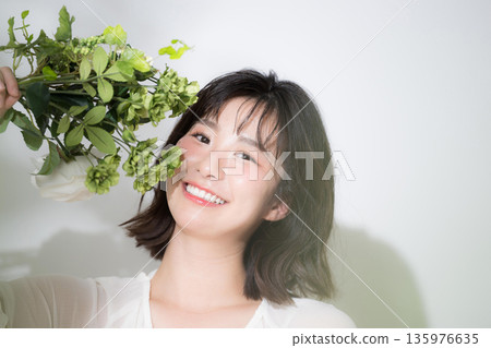 Spring image of holding a bouquet of fresh greenery. Beauty image for pre-wedding photoshoots and skincare. Looking at the camera. Spring image of holding a bouquet of fresh greenery. Beauty image for pre-wedding photoshoots and skincare. Looking at the camera. 135976635