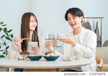 一對年輕的亞洲夫婦正在家裡的餐桌上享用美食。 一對年輕的亞洲夫婦正在家裡的餐桌上享用美食。 135976678