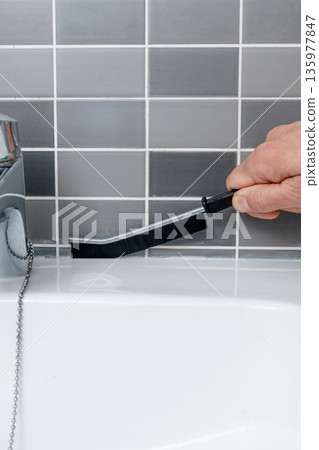 a man scrubs the joints along the sink tiles a man scrubs the joints along the sink tiles 135977847