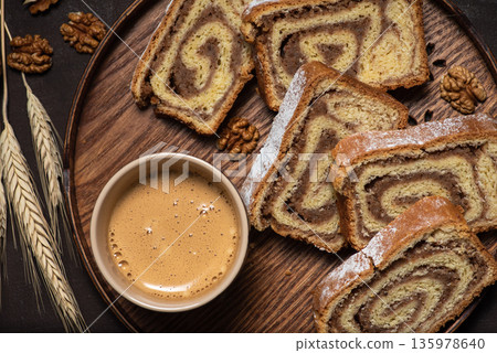 Pieces of homemade strudel with walnuts in a wooden tray and cup of coffee, close up 135978640