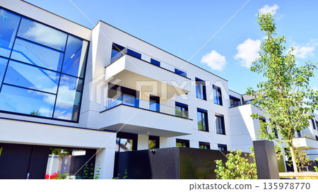 Modern architecture of urban residential apartment buildings on a sunny day. Low-rise apartment buildings with large windows and extensive terraces. White facade of a modern apartment building. 135978770