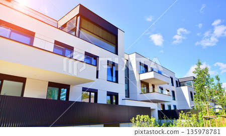Modern architecture of urban residential apartment buildings on a sunny day. Low-rise apartment buildings with large windows and extensive terraces. White facade of a modern apartment building. Modern architecture of urban residential apartment buildings on a sunny day. Low-rise apartment buildings with large windows and extensive terraces. White facade of a modern apartment building. 135978781