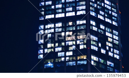 Big glowing windows in modern office building at night, in rows of windows light shines. Fragment of the glass facade of a modern corporate building at night. Modern glass office in city. Big glowing windows in modern office building at night, in rows of windows light shines. Fragment of the glass facade of a modern corporate building at night. Modern glass office in city. 135979453