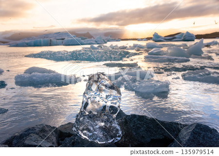 Icebergs float in Iceland's glacier lagoon, reflecting the warm colors of sunset. Birds fly above, adding life to the tranquil scene. This location is a must-see for nature enthusiasts. 135979514