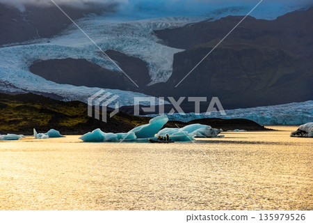 Fjallsarlon glacial lagoon showcases icebergs floating in calm waters, reflecting the soft twilight glow against the massive glacier backdrop. An iconic location in Iceland Fjallsarlon glacial lagoon showcases icebergs floating in calm waters, reflecting the soft twilight glow against the massive glacier backdrop. An iconic location in Iceland 135979526