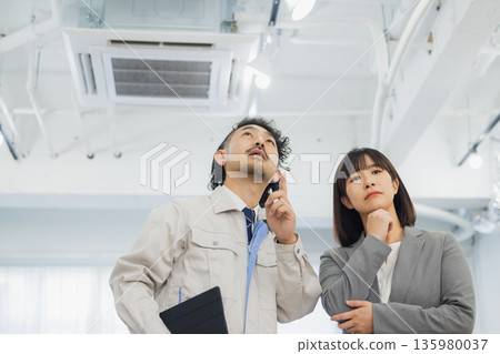 A businesswoman and a worker with dissatisfied expressions looking at the air conditioner 135980037