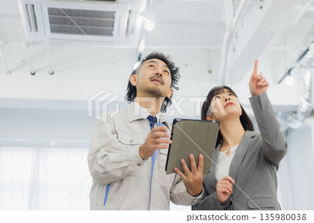一位女商人和一個工人面露不滿地看著空調。 一位女商人和一個工人面露不滿地看著空調。 135980038