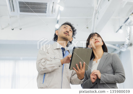 一位女商人和一個工人面露不滿地看著空調。 135980039