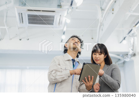 A businesswoman and a worker with dissatisfied expressions looking at the air conditioner A businesswoman and a worker with dissatisfied expressions looking at the air conditioner 135980040