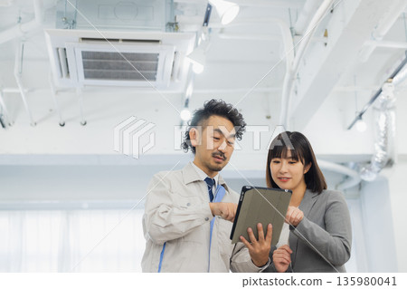 A businesswoman and a worker with dissatisfied expressions looking at the air conditioner 135980041