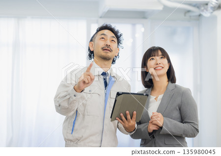 一位女商人和一個工人面露不滿地看著空調。 135980045