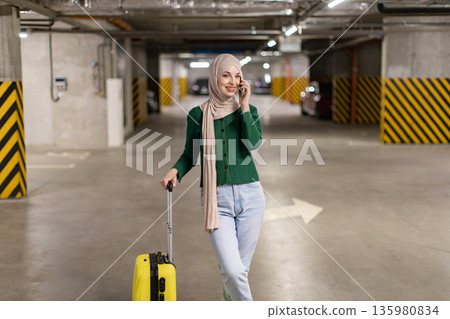 A woman wearing a hijab smiles while talking on her phone in an underground parking garage A woman wearing a hijab smiles while talking on her phone in an underground parking garage 135980834