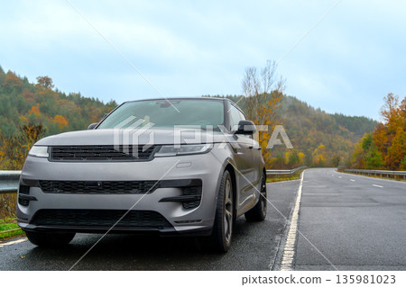 car on the road. Luxury SUV parked on the roadside under cloudy skies with green hills in the background during late autumn car on the road. Luxury SUV parked on the roadside under cloudy skies with green hills in the background during late autumn 135981023