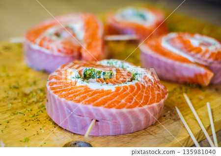 Cooked salmon rolls with creamy filling and herbs on a wooden board. Elegant seafood appetizer perfect for healthy cuisine, festive table, or restaurant presentation 135981040