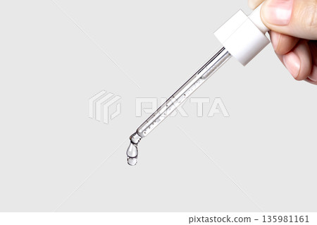 Pipette with serum in hand. Drips drop isolated on gray background, copy space photo close up 135981161