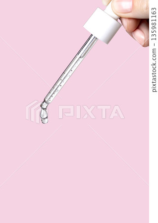 Pipette with serum in hand. Drips drop isolated on pink background, vertical photo copy space close up Pipette with serum in hand. Drips drop isolated on pink background, vertical photo copy space close up 135981163