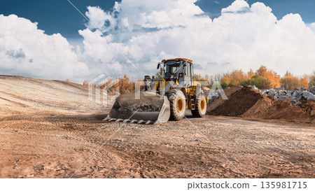 Loader is moving dirt on a construction site. The area is preparing for new structures with trees in the background and clouds overhead 135981715