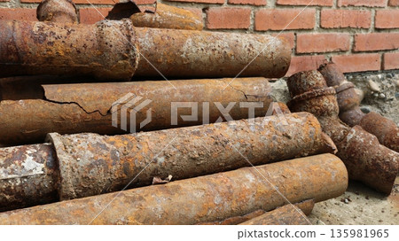 Old, used, rusty underground water pipes lying against the brick wall of a building, excavation of dilapidated water connections and excavations of house infrastructure Old, used, rusty underground water pipes lying against the brick wall of a building, excavation of dilapidated water connections and excavations of house infrastructure 135981965
