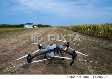 Drone in a farm field with corn on the right and a solar-powered building nearby for agricultural work 135982238
