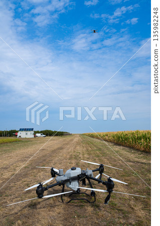 Drone on field ready for agricultural flight over corn field near a small solar-equipped building 135982248