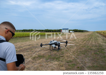 Drone on a rural field with operator, solar panel shed, and clear blue sky 135982250