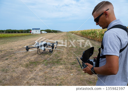 Drone pilot prepares agricultural drone in a cornfield for field surveillance and spraying. Drone pilot prepares agricultural drone in a cornfield for field surveillance and spraying. 135982397